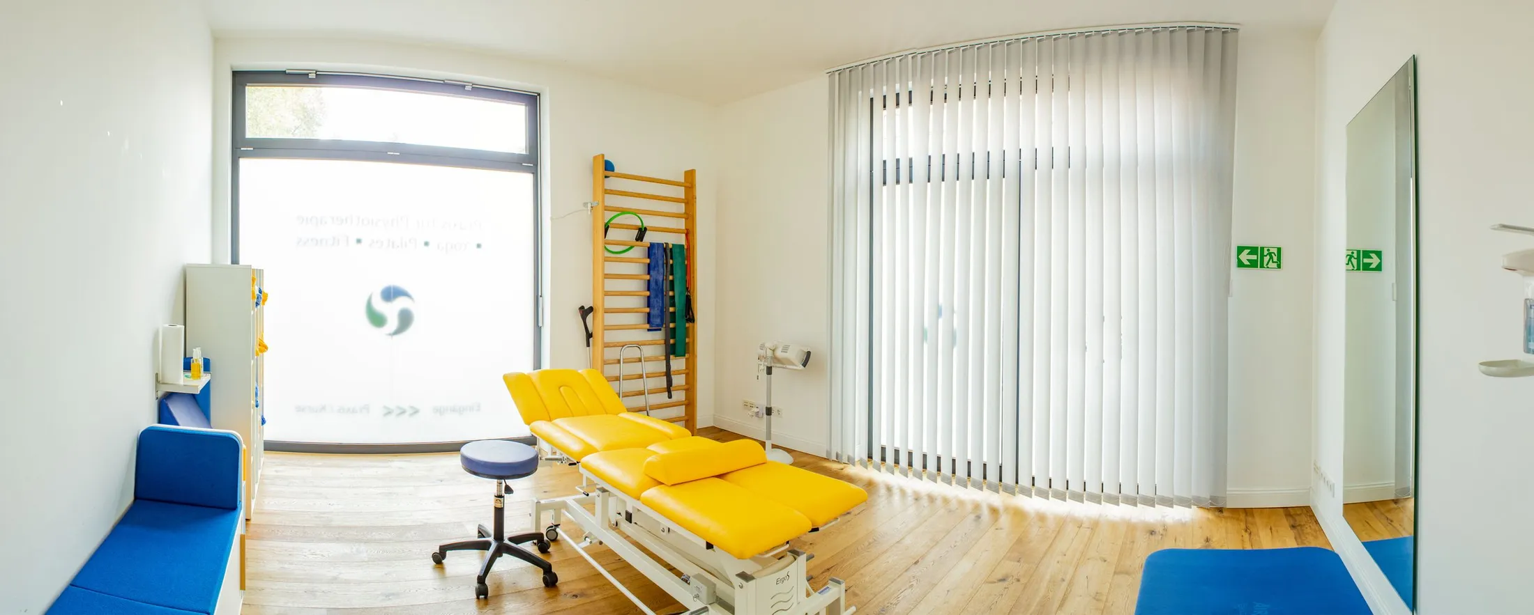 Heller Behandlungsraum mit Sprossenwand und Behandlungsliege